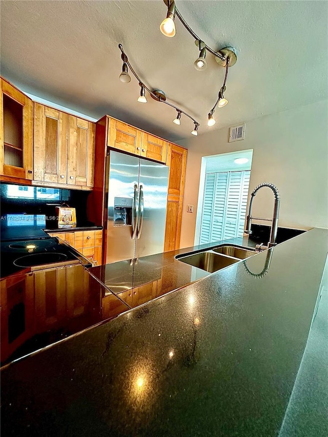 kitchen featuring visible vents, a sink, a textured ceiling, dark countertops, and stainless steel fridge