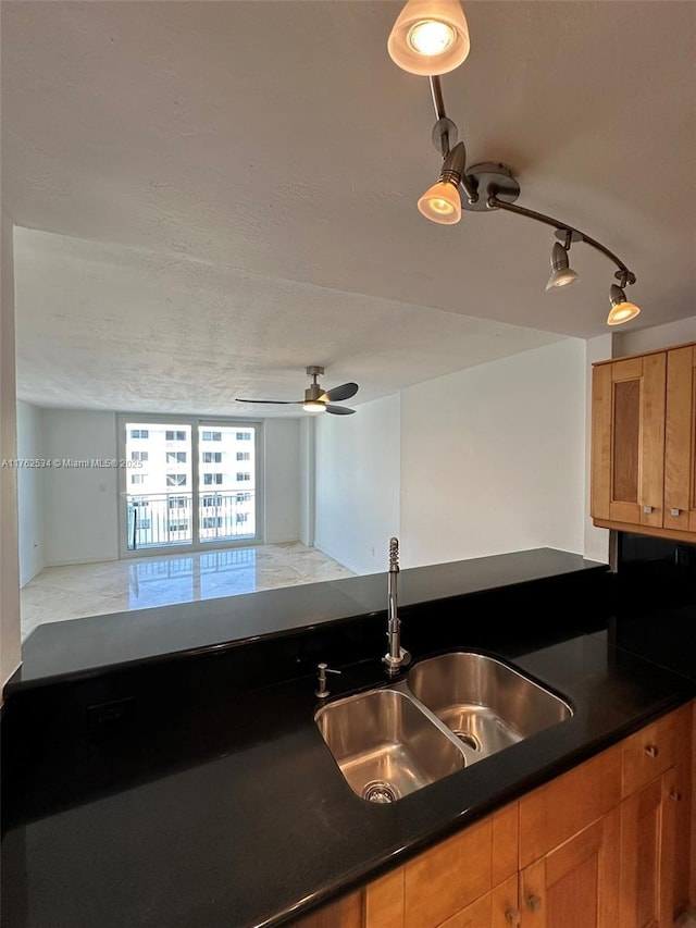 kitchen with a sink, a ceiling fan, dark countertops, and brown cabinetry