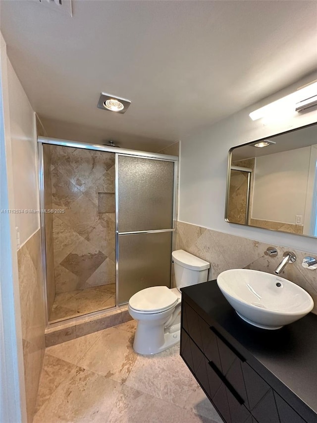 full bath featuring a wainscoted wall, toilet, vanity, a stall shower, and tile walls