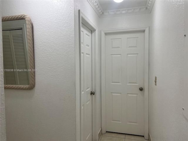 hallway with light tile patterned floors, a textured wall, and ornamental molding