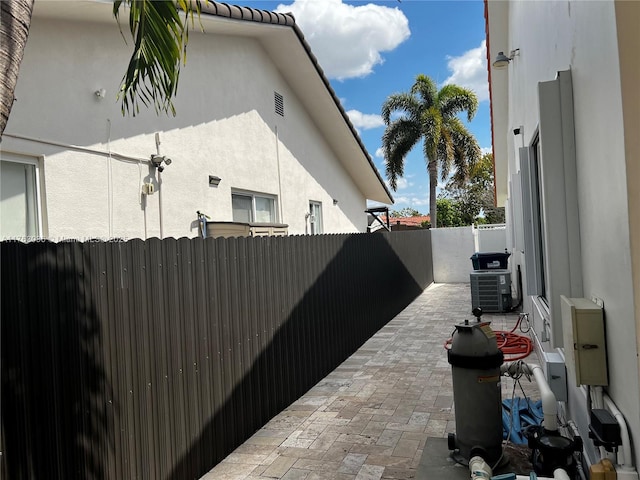 view of side of property with a tiled roof, stucco siding, cooling unit, a fenced backyard, and a patio area