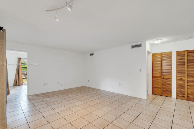spare room with light tile patterned floors, visible vents, and track lighting