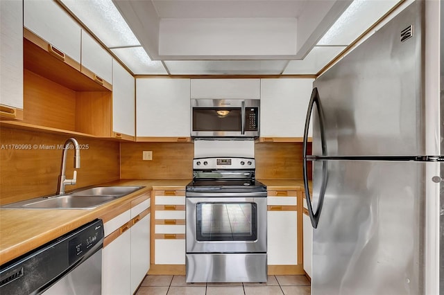 kitchen with a sink, appliances with stainless steel finishes, light tile patterned floors, and white cabinetry
