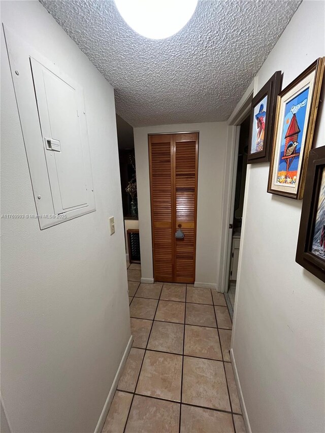 hall featuring electric panel, light tile patterned floors, a textured ceiling, and baseboards