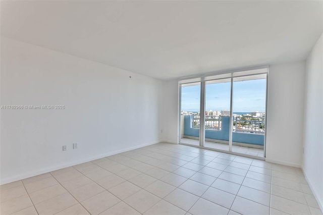 spare room with light tile patterned floors, a city view, floor to ceiling windows, and baseboards