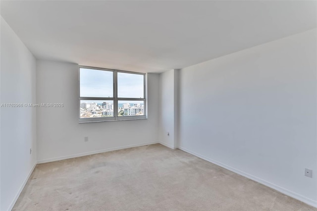 spare room featuring light carpet and baseboards