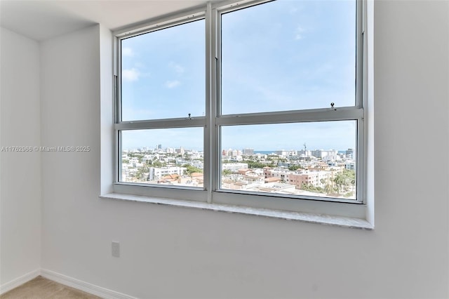 unfurnished room with carpet flooring, a view of city, and baseboards