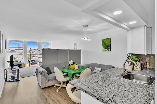 interior space with open floor plan, light wood-type flooring, decorative backsplash, white cabinets, and a sink