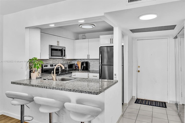 kitchen featuring a kitchen bar, decorative backsplash, appliances with stainless steel finishes, a peninsula, and white cabinets