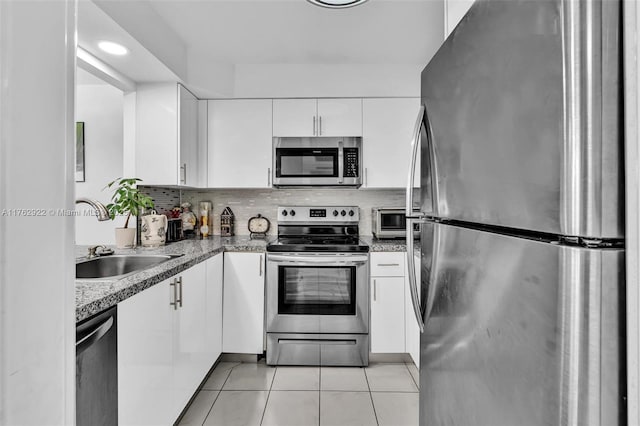 kitchen featuring light tile patterned floors, a sink, stainless steel appliances, white cabinets, and backsplash