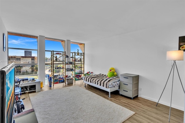 bedroom featuring a wall of windows, baseboards, and wood finished floors