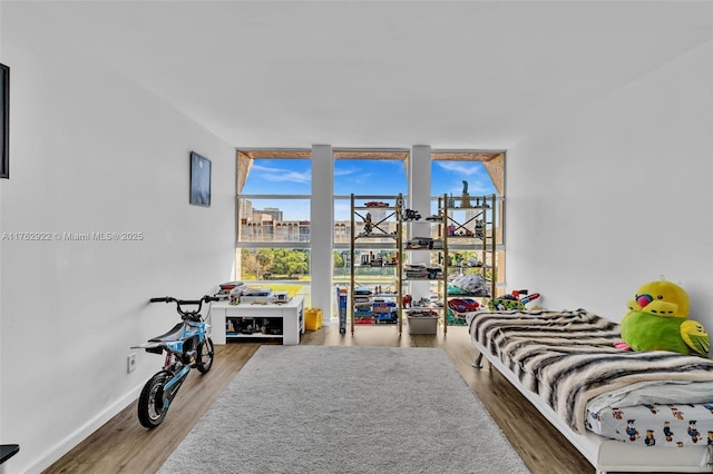 bedroom with a wall of windows, baseboards, wood finished floors, and a view of city