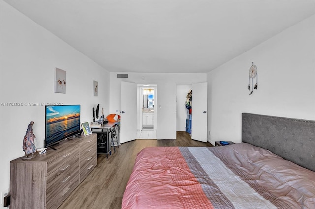 bedroom featuring wood finished floors, visible vents, and connected bathroom