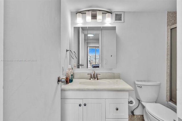 bathroom featuring vanity, toilet, visible vents, and a shower with door