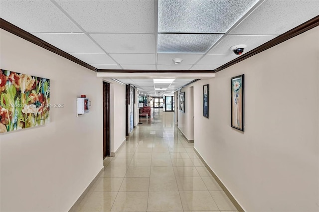 hall with light tile patterned floors, baseboards, and a drop ceiling