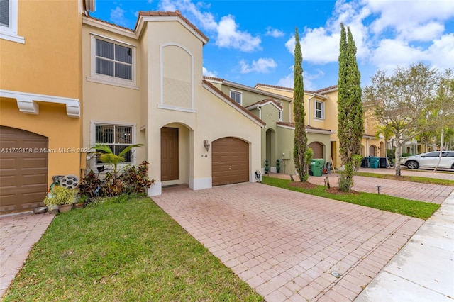 view of property with a front yard, stucco siding, a garage, a tile roof, and decorative driveway