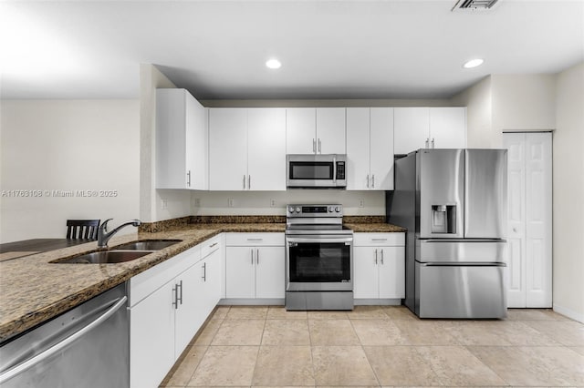 kitchen with a sink, stainless steel appliances, white cabinets, and dark stone counters