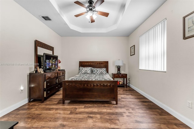 bedroom with visible vents, a raised ceiling, baseboards, and wood finished floors