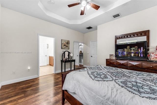 bedroom featuring visible vents, ensuite bathroom, a tray ceiling, wood finished floors, and baseboards