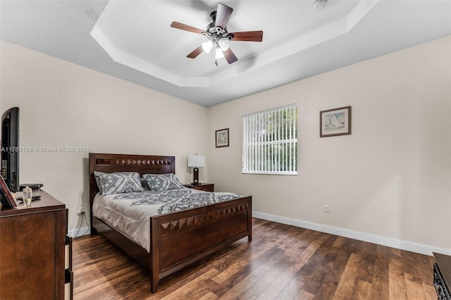 bedroom featuring a raised ceiling, baseboards, wood-type flooring, and ceiling fan