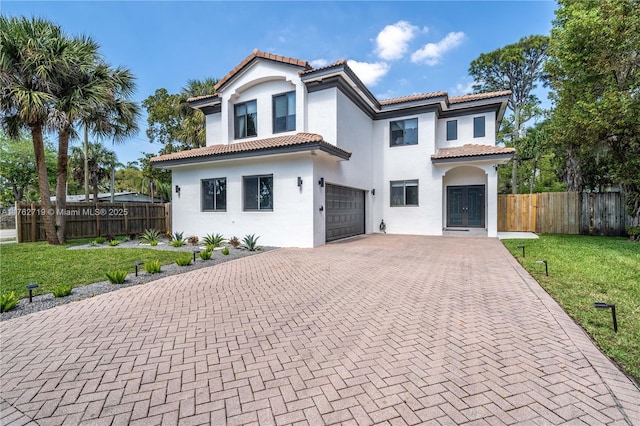 mediterranean / spanish-style house with stucco siding, a tile roof, decorative driveway, fence, and a garage