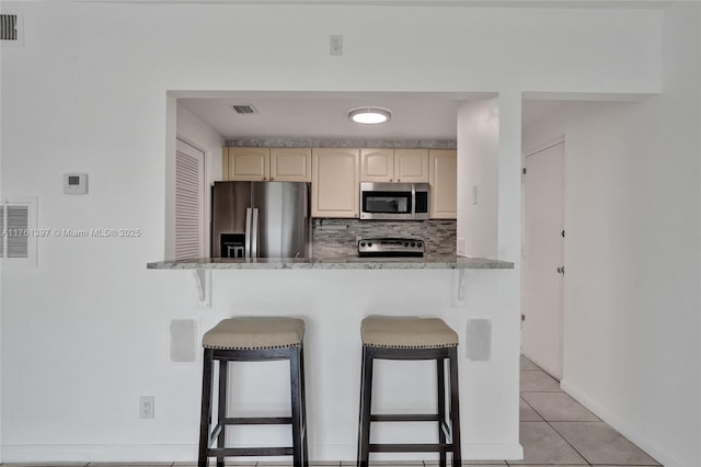 kitchen featuring a kitchen bar, visible vents, tasteful backsplash, appliances with stainless steel finishes, and light tile patterned flooring