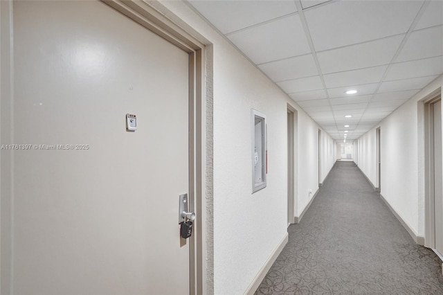 hallway with recessed lighting, dark carpet, a paneled ceiling, and baseboards