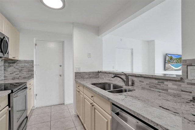 kitchen with a sink, light stone counters, backsplash, appliances with stainless steel finishes, and light tile patterned floors