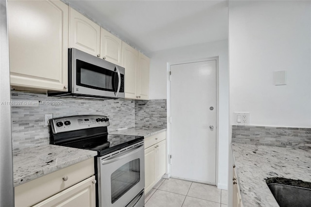 kitchen featuring light tile patterned flooring, decorative backsplash, appliances with stainless steel finishes, and light stone countertops