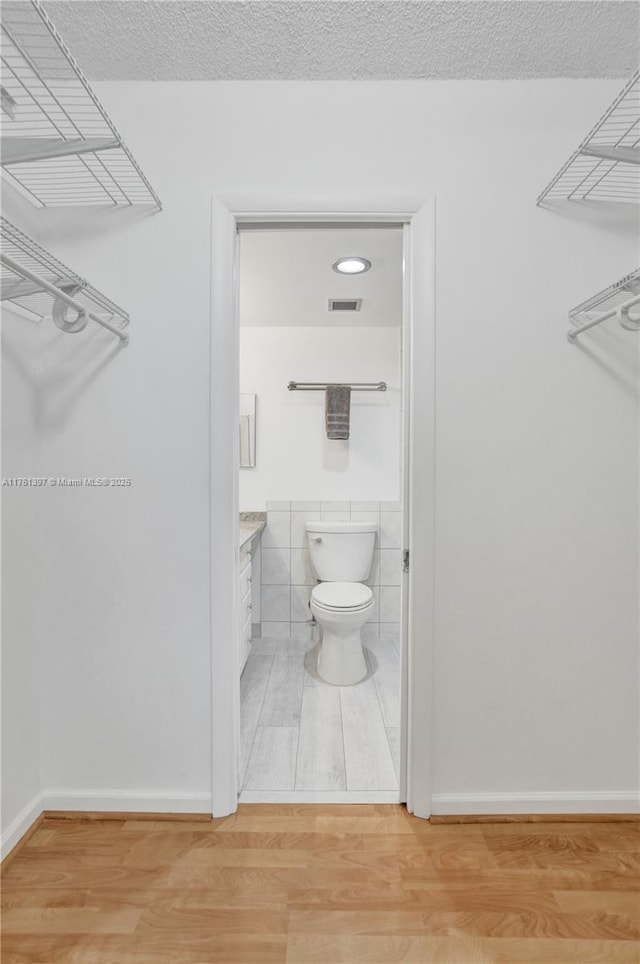 interior space with toilet, a textured ceiling, wood finished floors, tile walls, and vanity