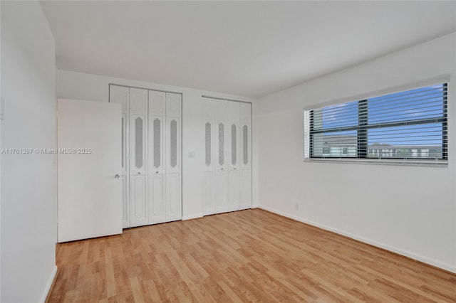 unfurnished bedroom featuring baseboards, light wood-type flooring, and two closets