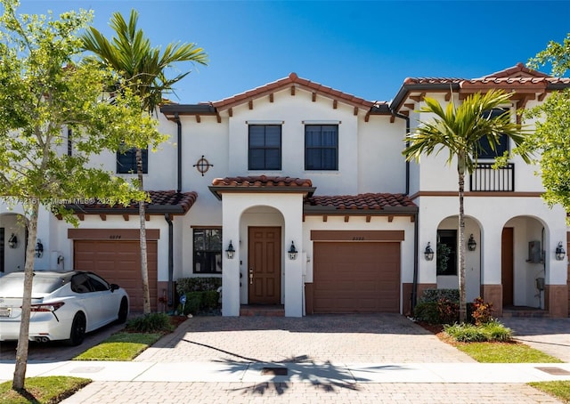 mediterranean / spanish house featuring a tiled roof, stucco siding, driveway, a balcony, and an attached garage