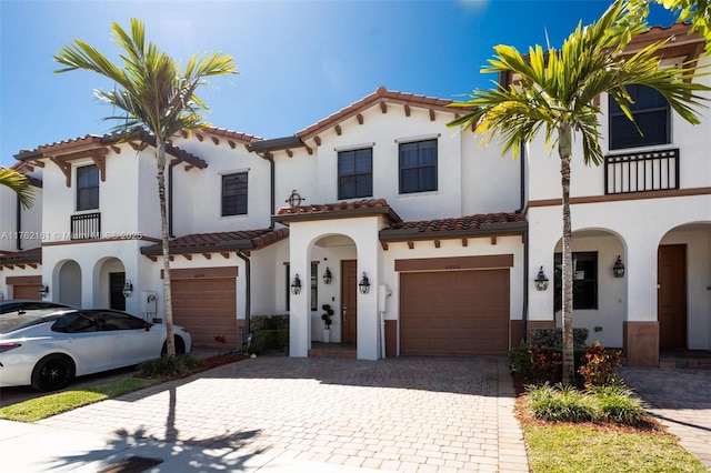 mediterranean / spanish-style house with a tile roof, stucco siding, decorative driveway, a balcony, and a garage