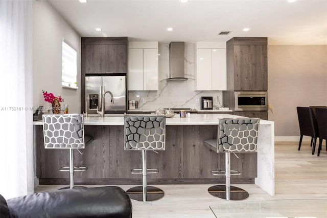 kitchen with a breakfast bar, stainless steel appliances, wall chimney range hood, and modern cabinets