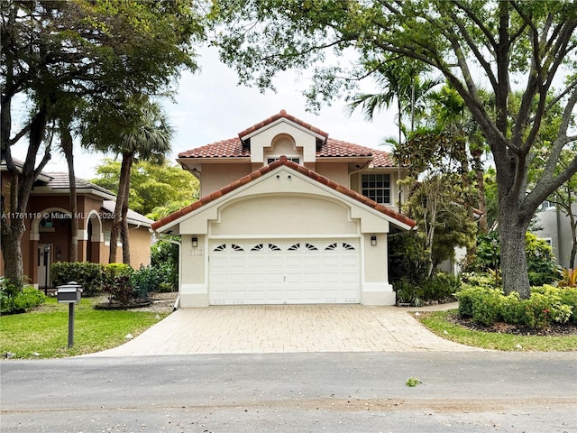 mediterranean / spanish-style home with a garage, decorative driveway, a tile roof, and stucco siding