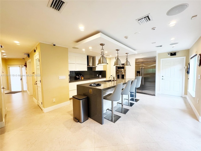 kitchen featuring a sink, wall chimney range hood, visible vents, and stainless steel built in refrigerator