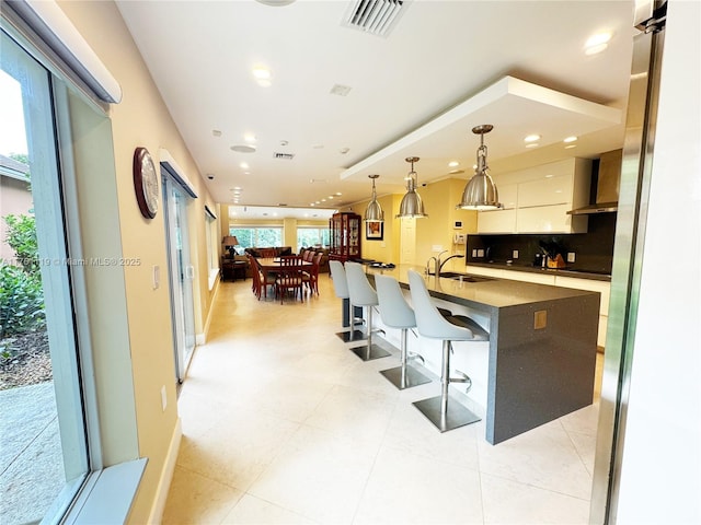 kitchen with visible vents, a sink, a kitchen bar, dark countertops, and tasteful backsplash