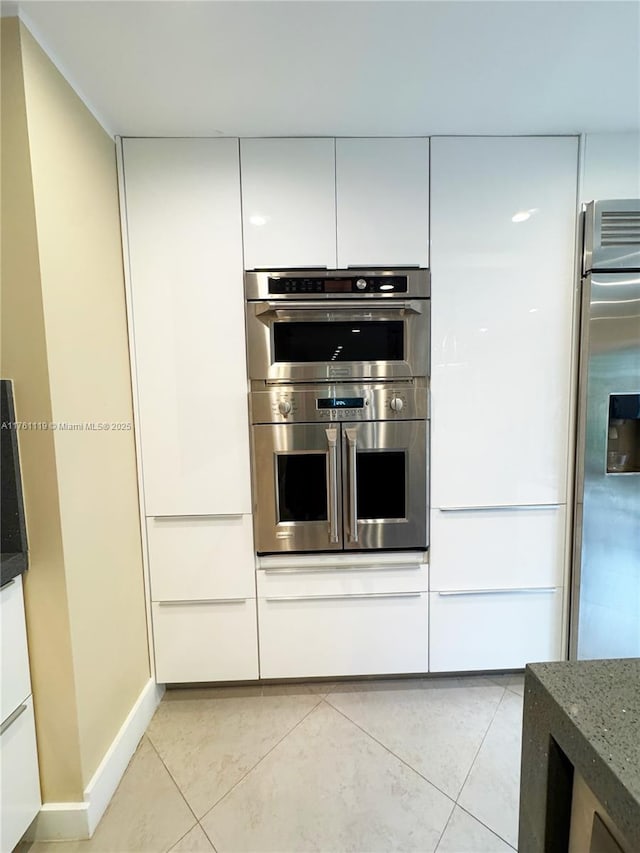 kitchen featuring light tile patterned floors, dark stone counters, appliances with stainless steel finishes, and white cabinetry