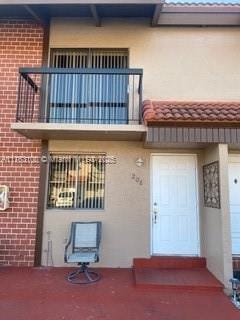 doorway to property featuring a tiled roof, a balcony, brick siding, and stucco siding