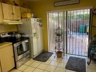 kitchen featuring light tile patterned flooring, white fridge with ice dispenser, under cabinet range hood, and stainless steel range with electric cooktop