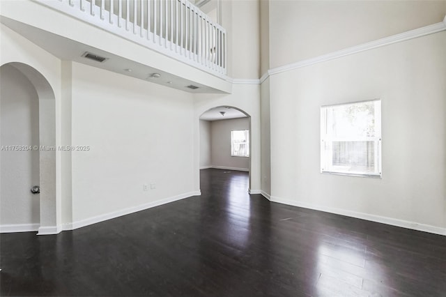 unfurnished room featuring visible vents, dark wood-type flooring, arched walkways, a high ceiling, and baseboards