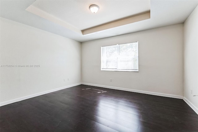 empty room featuring a tray ceiling, baseboards, and dark wood-type flooring