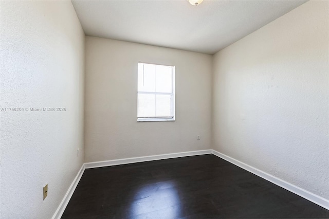 unfurnished room with a textured wall, baseboards, and dark wood-style flooring