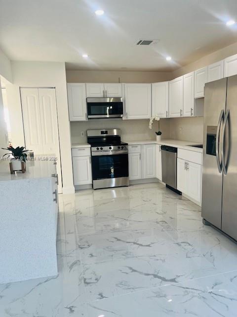 kitchen with marble finish floor, appliances with stainless steel finishes, light countertops, and white cabinetry