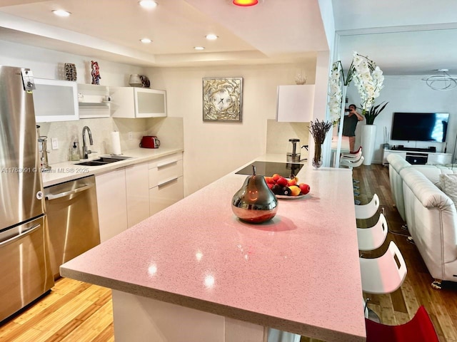 kitchen with light wood-type flooring, appliances with stainless steel finishes, white cabinetry, a raised ceiling, and a sink