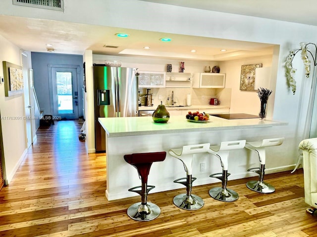 kitchen featuring light wood-type flooring, visible vents, a peninsula, a breakfast bar area, and stainless steel fridge with ice dispenser