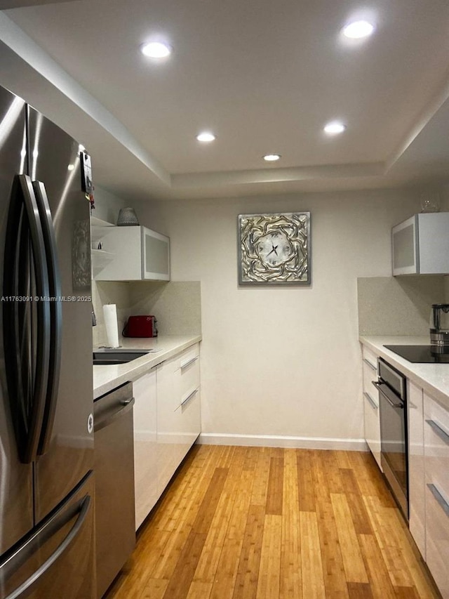 kitchen featuring light wood-type flooring, black appliances, light countertops, and a tray ceiling