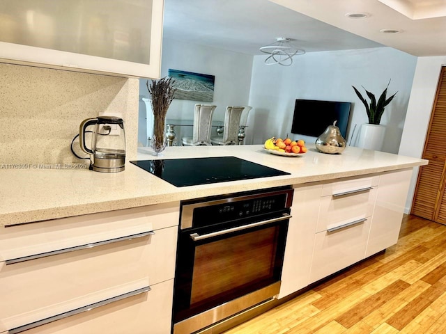 kitchen featuring modern cabinets, white cabinetry, light wood-style floors, stainless steel oven, and black electric cooktop