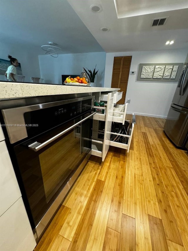 interior space with visible vents, light wood-style flooring, freestanding refrigerator, wine cooler, and baseboards