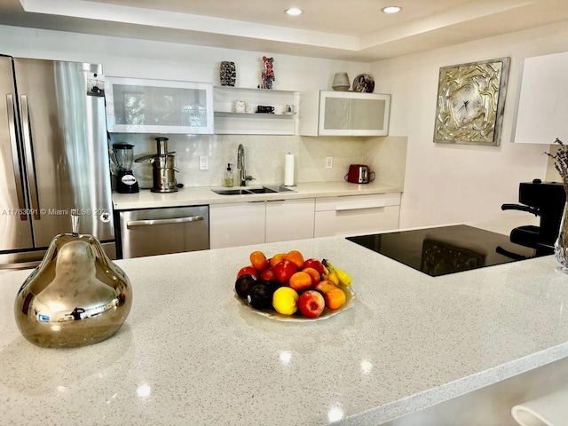 kitchen featuring light stone counters, a sink, decorative backsplash, appliances with stainless steel finishes, and white cabinetry